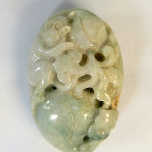 May include: A green jade carving of a dragon with intricate details. The carving is oval shaped and has a smooth, polished finish.