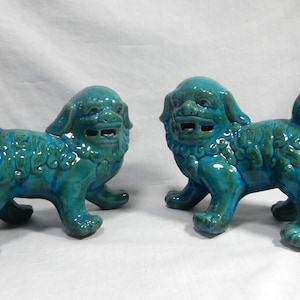Puede incluir: Dos estatuas de cerámica turquesa de perros Foo. Estas figuras decorativas presentan un diseño detallado con un acabado brillante. Los perros Foo están de pie con la boca abierta y la cola enroscada.