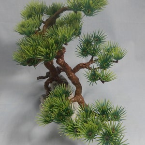 Op de afbeelding: Kunstmatige bonsai boom met groene naalden en bruine takken. De boom is bevestigd op een witte rotsbasis. De takken zijn kunstzinnig gerangschikt, waardoor de indruk van een miniatuurboom ontstaat. Het ontwerp is bedoeld voor decoratieve doeleinden.