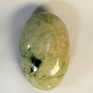 May include: A smooth, oval-shaped green jade stone with white and brown swirls and a dark green spot.