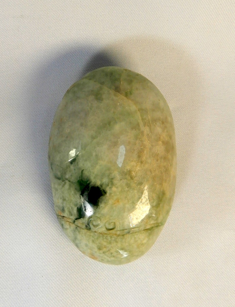 May include: A smooth, oval-shaped green jade stone with white and brown swirls and a dark green spot.