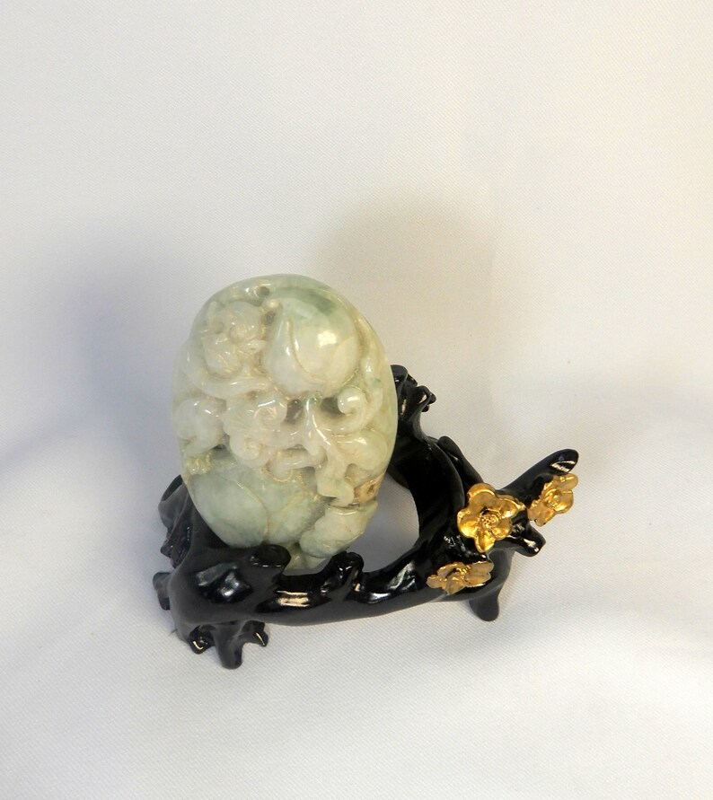 May include: A carved jade egg with intricate details, resting on a black wooden stand with gold accents. The stand is shaped like a tree branch with stylised flowers.
