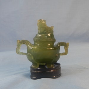 Puede incluir: Un pequeño quemador de incienso de jade verde con un remate de dragón, sentado sobre una base de madera negra.