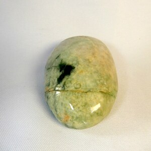 May include: A smooth, oval-shaped green and white stone with a darker green patch. The stone has a glossy finish.