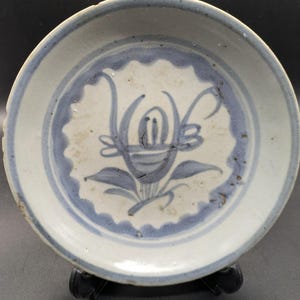 Peut inclure: Petite assiette ronde en céramique antique, blanche et ornée d'un motif floral bleu. Bordure bleue festonnée et motif floral central bleu. L'assiette est probablement vintage et présente des signes d'usure.