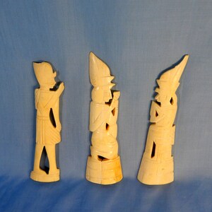 Puede incluir: Tres tallas de marfil de figuras con vestimenta tradicional. Las figuras est&aacute;n de pie sobre una superficie azul claro.