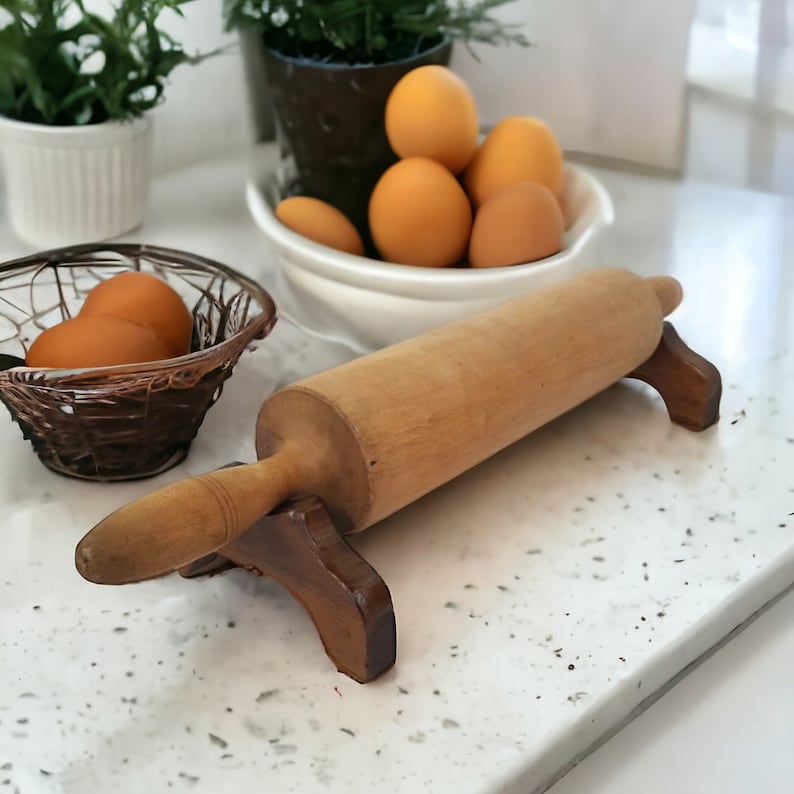 May include: A wooden rolling pin with a wooden stand on a white countertop. There are eggs in a basket and a bowl of eggs in the background.