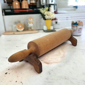 May include: A wooden rolling pin with a brown wooden stand. The rolling pin is resting on a white surface with a light brown powder.