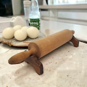 May include: A wooden rolling pin with a brown handle and wooden stand. The rolling pin is on a white countertop with white and brown ceramic tiles.