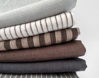 May include: A stack of six folded fabric pieces featuring various textures and patterns. The collection includes solid light gray, white with thin brown stripes, wide brown and beige stripes, solid dark brown, solid charcoal gray, and charcoal gray with thin white stripes.