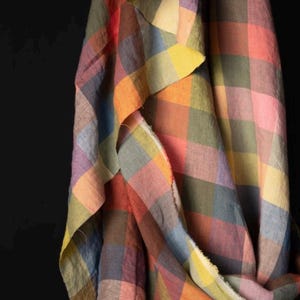 May include: A draped fabric with a colorful plaid pattern. The fabric features a mix of colors including pink, orange, yellow, green, blue, and purple. The fabric is likely linen or a similar lightweight material.