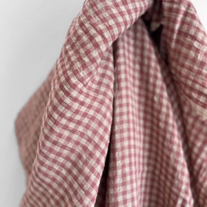 May include: Close-up of a fabric with a red and white gingham pattern. The fabric is draped, showing the texture and folds of the material. The color palette is soft and inviting, with a classic, timeless appeal.