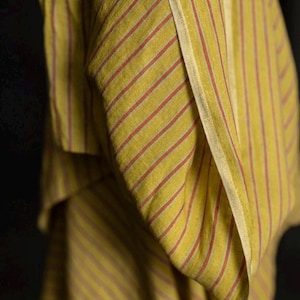 May include: Close-up of a yellow and red striped fabric. The fabric has vertical stripes of yellow and thin red lines. The fabric is folded, showing the texture and pattern. The background is dark.