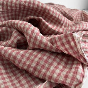 May include: A close-up of a red and white gingham fabric. The fabric is draped and folded, creating a textured appearance. The pattern is a classic checkered design, with the red and white squares evenly spaced.