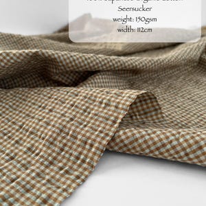 May include: Toffee and mint coloured seersucker fabric featuring a small checkered pattern. The textile is labelled as 100% Japanese organic cotton with a weight of 150gsm and a width of 112cm. The material has a puckered, textured surface.