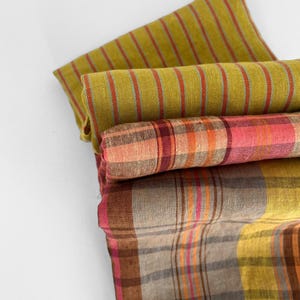 May include: A stack of folded fabric in shades of green, pink, and brown. The top fabric has vertical stripes in red and orange. The middle fabric has a plaid pattern in pink and orange. The bottom fabric has a plaid pattern in brown, yellow, and pink.