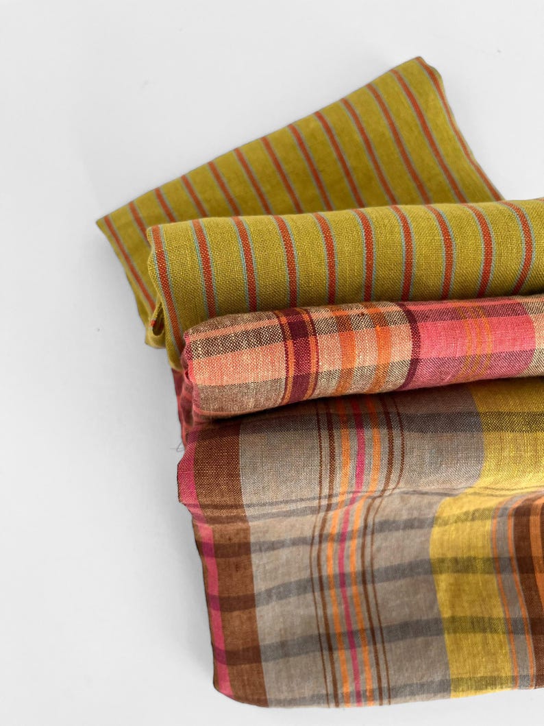 May include: A stack of folded fabric in shades of green, pink, and brown. The top fabric has vertical stripes in red and orange. The middle fabric has a plaid pattern in pink and orange. The bottom fabric has a plaid pattern in brown, yellow, and pink.
