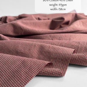 May include: Fabric with a very berry micro check pattern, composed of 60% cotton and 40% linen. The material has a weight of 115gsm and a width of 138cm. The textile features a small-scale checkered design in muted reddish-pink and dark tones.