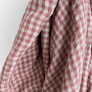 May include: Close-up of a draped fabric with a red and white checkered pattern. The fabric appears to be linen or a similar lightweight material, with a soft, textured appearance. The checks are evenly sized and create a classic, timeless design.