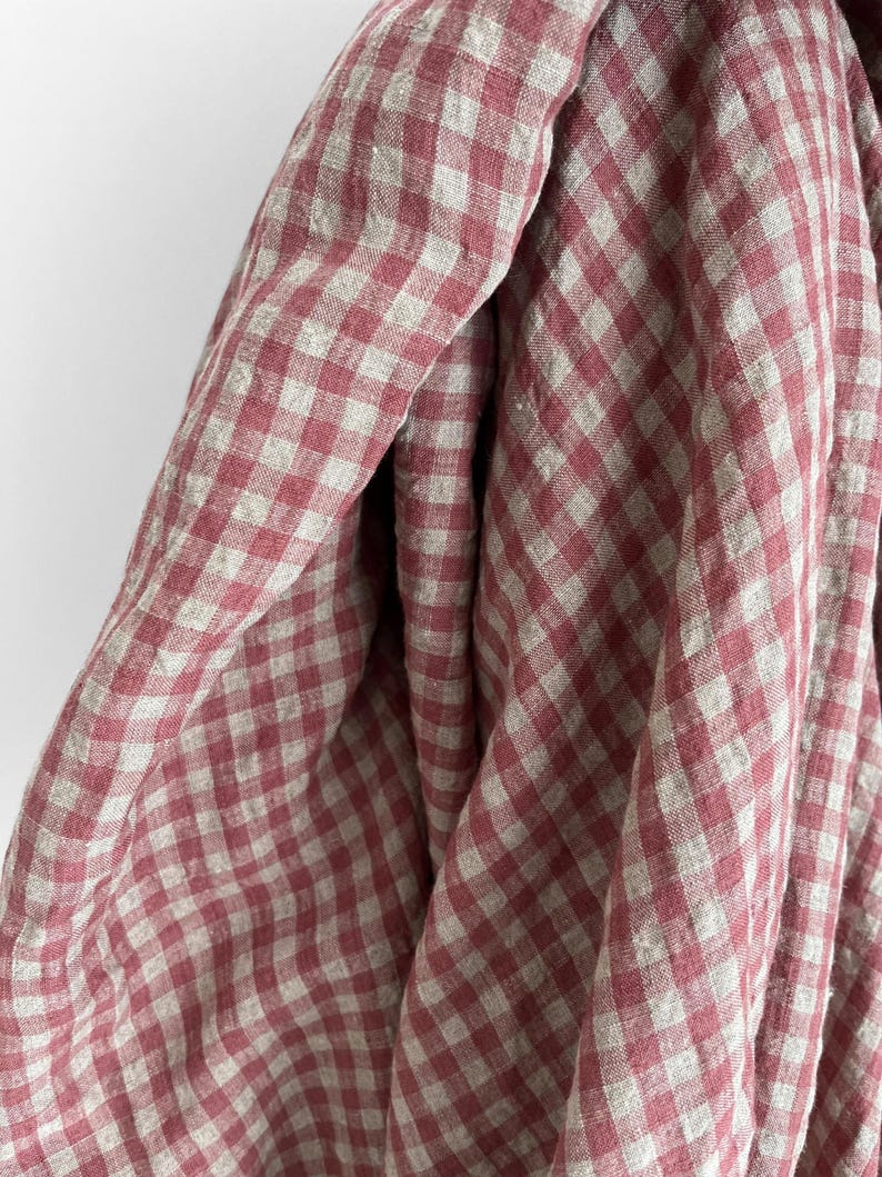 May include: Close-up of a draped fabric with a red and white checkered pattern. The fabric appears to be linen or a similar lightweight material, with a soft, textured appearance. The checks are evenly sized and create a classic, timeless design.