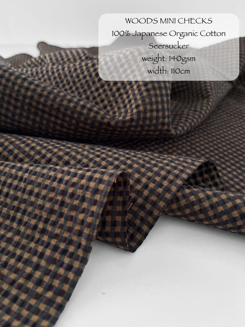 May include: A brown and black mini check seersucker fabric made of 100% Japanese organic cotton. The textile features a puckered texture and is labelled as WOODS MINI CHECKS, 100% Japanese Organic Cotton Seersucker, weight: 140gsm, width: 110cm.