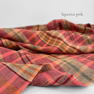 May include: A close-up of a fabric with a plaid pattern in shades of pink, orange, green, and brown. The fabric is draped, with the words "liquorice pink" in a script font.
