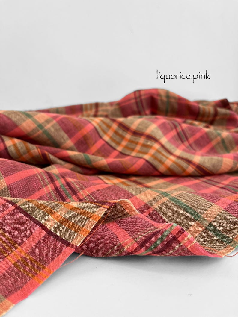 May include: A close-up of a fabric with a plaid pattern in shades of pink, orange, green, and brown. The fabric is draped, with the words "liquorice pink" in a script font.