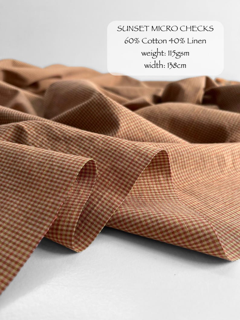 May include: Fabric with a sunset micro check pattern in shades of orange and cream. The text reads: SUNSET MICRO CHECKS, 60% Cotton 40% Linen, weight: 115gsm, width: 138cm. The material is draped in soft folds, showing a fine, woven texture.