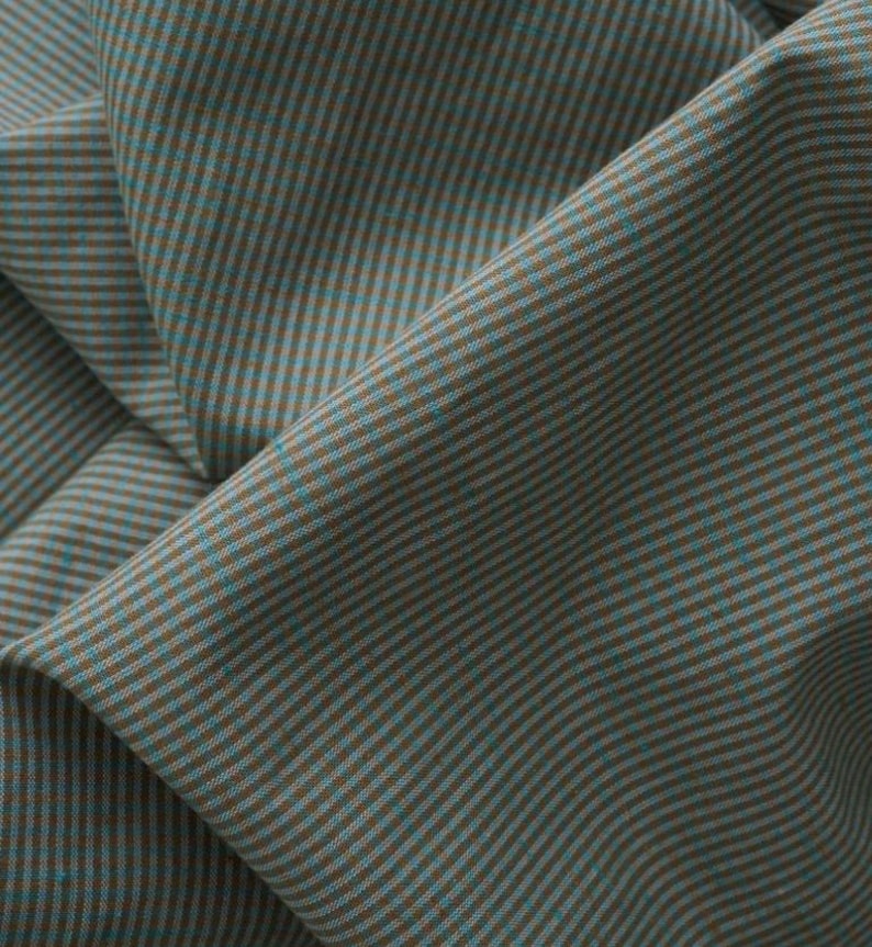 May include: A piece of fabric featuring a fine, repeating pinstripe pattern in alternating shades of muted teal and warm brown. The material is draped to show soft folds and shadows, highlighting the consistent vertical line texture throughout.