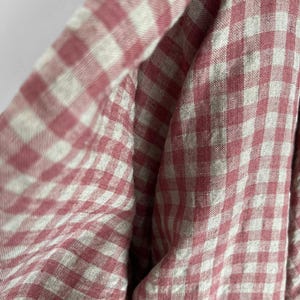 May include: Close-up of a fabric with a pink and white gingham pattern. The fabric is folded, creating soft curves and shadows. The pattern is a classic, timeless design, perfect for apparel or home decor.