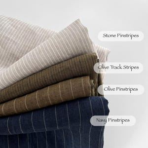 May include: A selection of fabric swatches in shades of beige, olive green, and navy blue, each with a striped pattern. The labels read 'Stone Pinstripes', 'Olive Track Stripes', 'Olive Pinstripes', and 'Navy Pinstripes'. The fabrics are neatly folded.