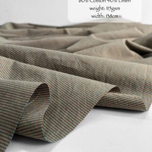 May include: Riviera Micro Checks fabric featuring a brown and teal micro-check pattern. The text reads: RIVIERA MICRO CHECKS, 60% Cotton 40% Linen, weight: 115gsm, width: 138cm. The fabric is draped in soft folds, showing a fine, woven texture.