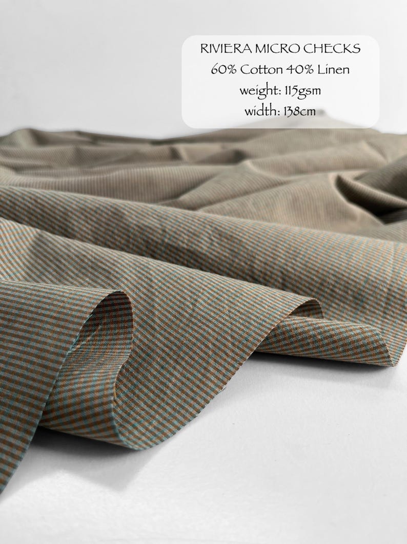 May include: Riviera Micro Checks fabric featuring a brown and teal micro-check pattern. The text reads: RIVIERA MICRO CHECKS, 60% Cotton 40% Linen, weight: 115gsm, width: 138cm. The fabric is draped in soft folds, showing a fine, woven texture.