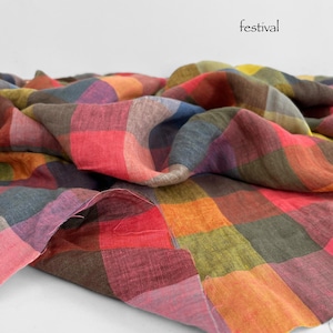 May include: A colorful, checkered fabric in shades of red, orange, green, and purple. The word "festival" is printed in black on the white background. The fabric is folded and draped, showcasing its texture and pattern.