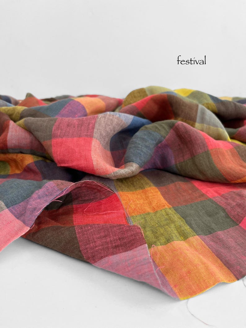 May include: A colorful, checkered fabric in shades of red, orange, green, and purple. The word "festival" is printed in black on the white background. The fabric is folded and draped, showcasing its texture and pattern.