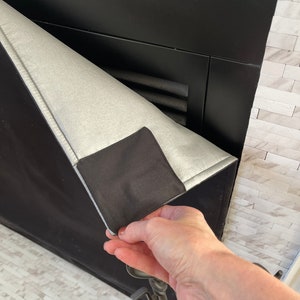 May include: A black fireplace screen with a silver fabric cover. The cover is being pulled up to reveal the black metal screen behind it.