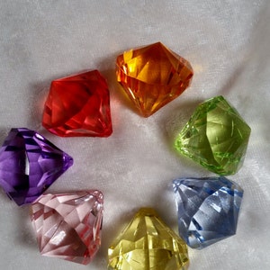 May include: Seven colorful faceted glass gems in the shape of diamonds. The gems are arranged in a circle on a white background. The colors of the gems are red, orange, yellow, green, blue, purple, and pink.