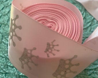 May include: Pink satin ribbon with silver glitter crown designs. The ribbon is rolled up and ready to be used for crafts or decorations.