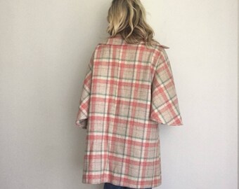 Puede incluir: Un abrigo vintage a cuadros en beige, rojo y verde. El abrigo tiene un cuello clásico y mangas anchas. La persona que lleva el abrigo está de espaldas a la cámara, con vaqueros azules.