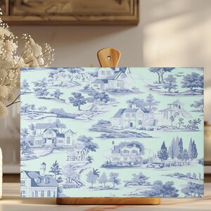 Peut inclure: Planche à découper rectangulaire avec une poignée en bois. Elle présente un motif de toile de Jouy bleu et blanc représentant des maisons et des paysages. Posée sur un comptoir clair.