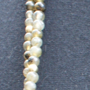 May include: A gold necklace with a large, round pendant. The necklace is made of multiple strands of small, round, white and grey beads.