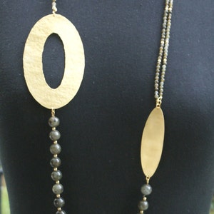 May include: A gold necklace with two oval-shaped pendants and a strand of dark grey beads.