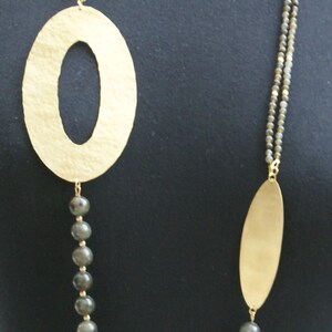 May include: A gold necklace with two oval pendants and grey beads. The necklace is on a black background.