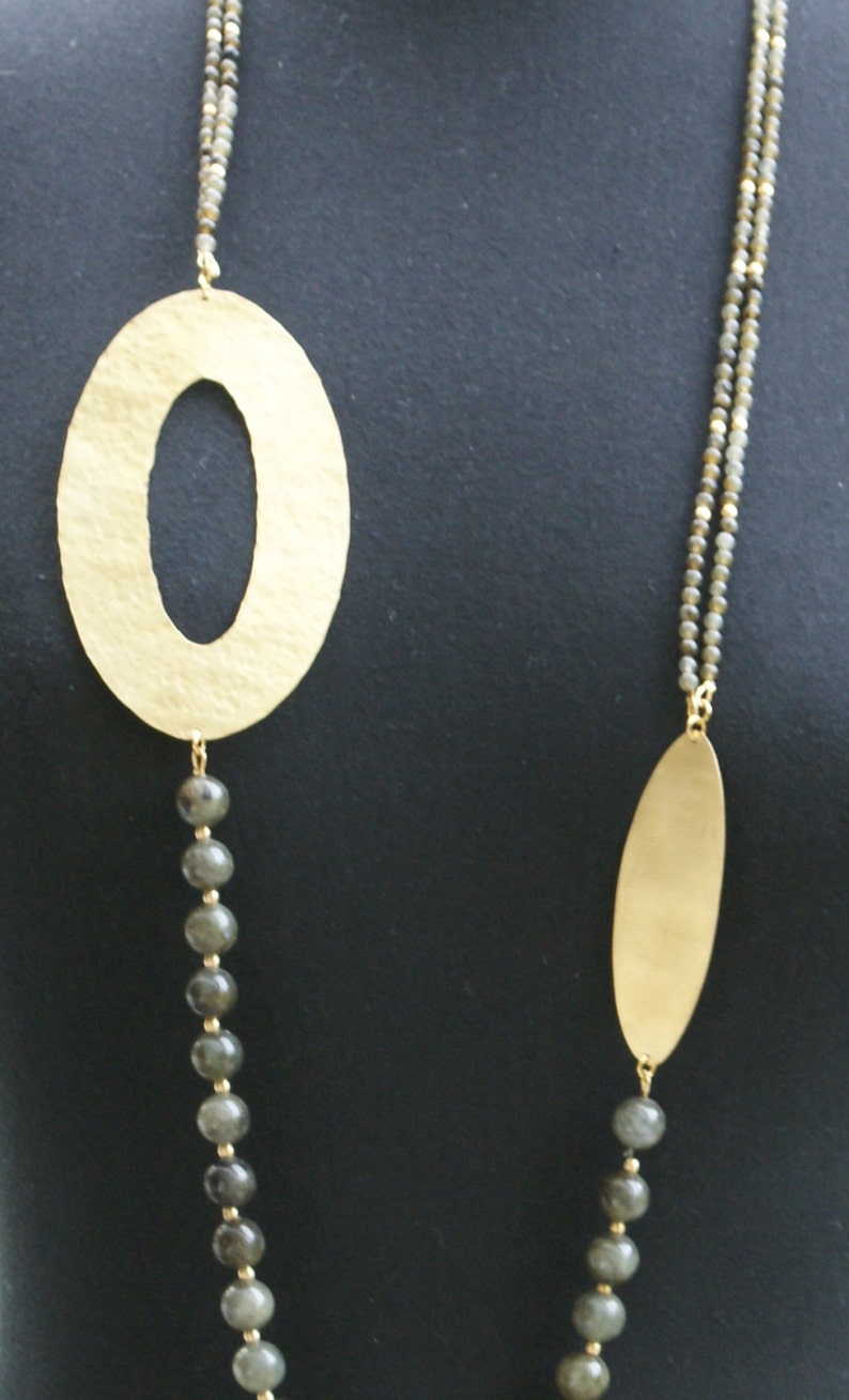 May include: A gold necklace with two oval pendants and grey beads. The necklace is on a black background.