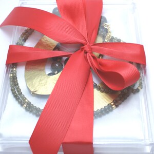 May include: A clear acrylic box with a red ribbon bow, containing a gold necklace with grey beads and a gold pendant.