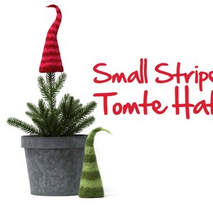 May include: Two small striped knit gnome hats. The larger hat is red and white and is on top of a small potted evergreen tree. The smaller hat is green and white and is on the table next to the tree. The text "Small Striped Tomte Hats" is written in red letters on a white background.