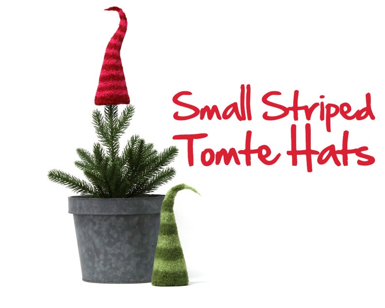 May include: Two small striped knit gnome hats. The larger hat is red and white and is on top of a small potted evergreen tree. The smaller hat is green and white and is on the table next to the tree. The text "Small Striped Tomte Hats" is written in red letters on a white background.