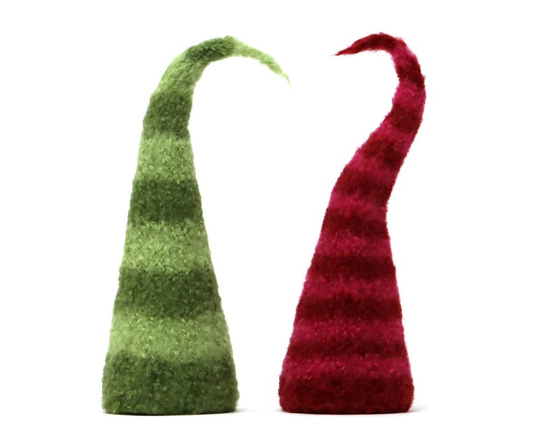 May include: Two felt elf hats, one green and one red, with white stripes. The hats are standing upright on a white background.