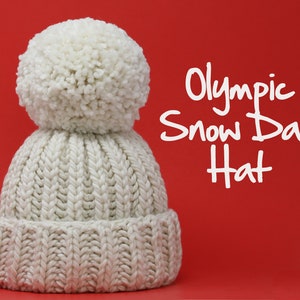 May include: A white knitted hat with a large white pom-pom on top. The hat is on a red background and the text "Olympic Snow Day Hat" is written in white letters.