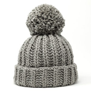 May include: A gray knitted beanie with a fluffy pom pom on top. The beanie has a ribbed texture.